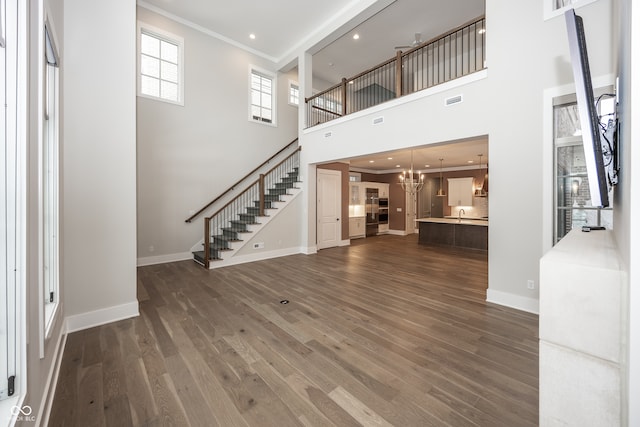 unfurnished living room with a towering ceiling, dark wood-type flooring, ornamental molding, and a chandelier