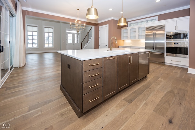 kitchen with stainless steel appliances, sink, white cabinetry, a center island with sink, and pendant lighting