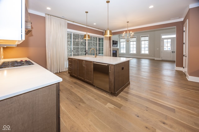 kitchen with sink, stainless steel appliances, light hardwood / wood-style floors, hanging light fixtures, and a center island with sink