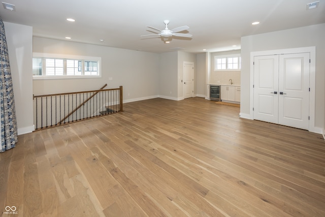 basement featuring light hardwood / wood-style floors, ceiling fan, and wine cooler