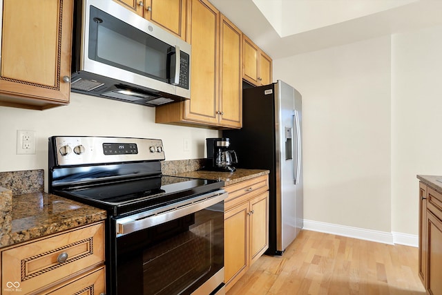 kitchen featuring dark stone countertops, light hardwood / wood-style floors, and appliances with stainless steel finishes