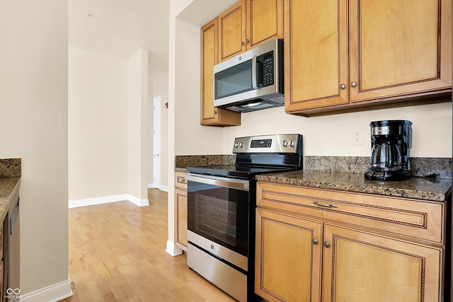 kitchen featuring dark stone countertops, light hardwood / wood-style flooring, and appliances with stainless steel finishes