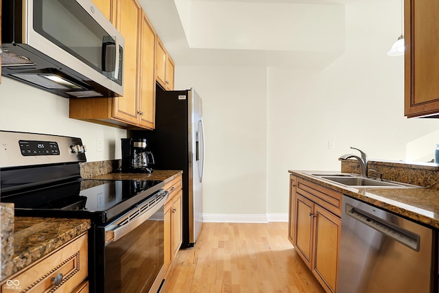 kitchen with light wood-type flooring, stainless steel appliances, dark stone countertops, and sink