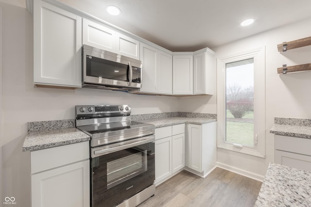 kitchen with light stone counters, white cabinetry, appliances with stainless steel finishes, and light hardwood / wood-style flooring