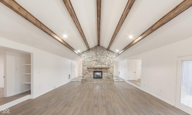 unfurnished living room with a wealth of natural light, a stone fireplace, built in features, lofted ceiling with beams, and hardwood / wood-style floors