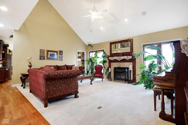 living room featuring light hardwood / wood-style floors, high vaulted ceiling, ceiling fan, and a tiled fireplace