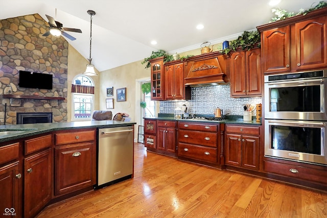 kitchen featuring lofted ceiling, backsplash, a stone fireplace, light hardwood / wood-style flooring, and stainless steel appliances