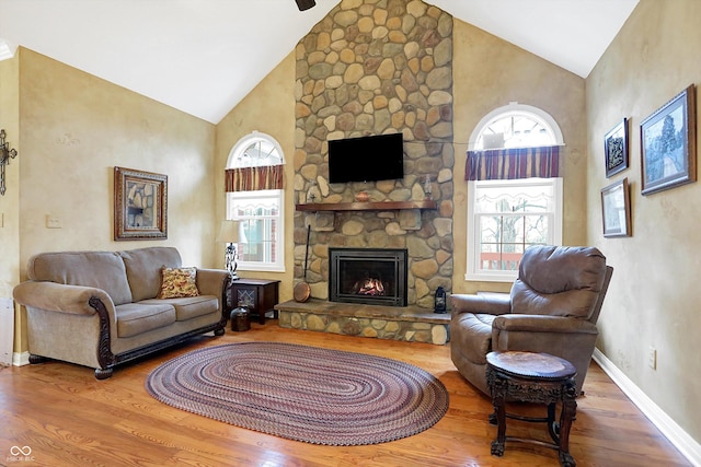 living room with hardwood / wood-style flooring, a stone fireplace, and high vaulted ceiling