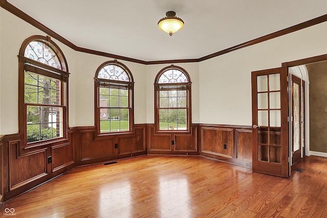 unfurnished room featuring visible vents, ornamental molding, light wood finished floors, and wainscoting