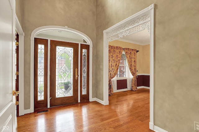 foyer entrance with baseboards, visible vents, ornamental molding, and wood finished floors