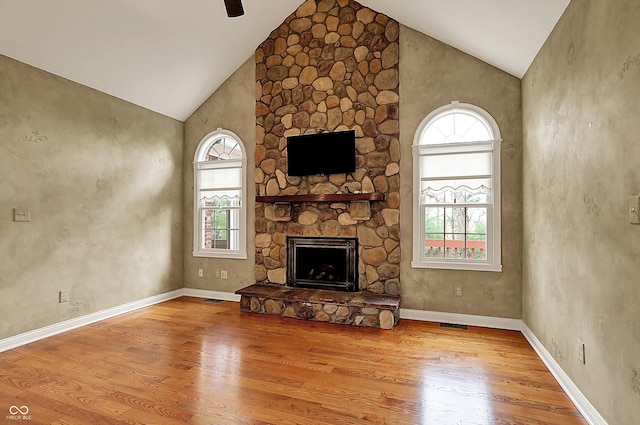 unfurnished living room with visible vents, wood finished floors, a stone fireplace, ceiling fan, and high vaulted ceiling