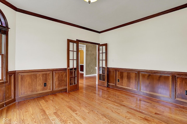 empty room with french doors, ornamental molding, light wood-style flooring, and a wainscoted wall
