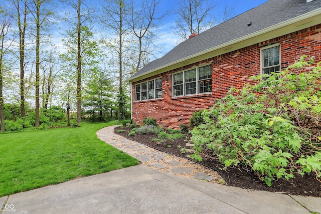 view of side of property featuring brick siding, roof with shingles, and a yard