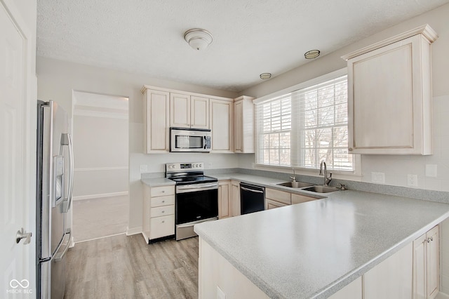 kitchen featuring sink, light wood-type flooring, a textured ceiling, appliances with stainless steel finishes, and kitchen peninsula