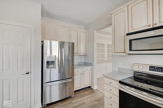 kitchen with appliances with stainless steel finishes, a textured ceiling, light hardwood / wood-style floors, and cream cabinets