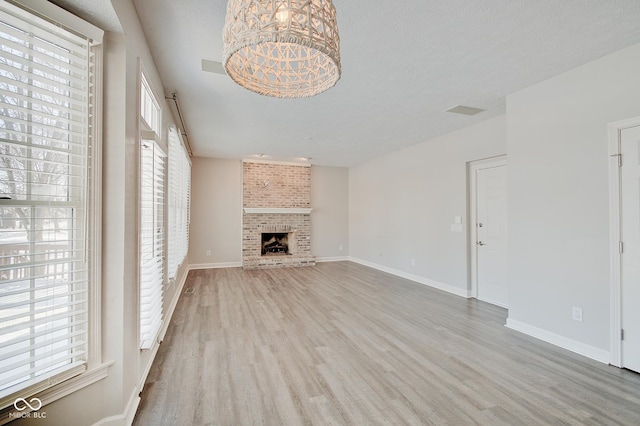 unfurnished living room with a brick fireplace, a textured ceiling, light hardwood / wood-style floors, and an inviting chandelier