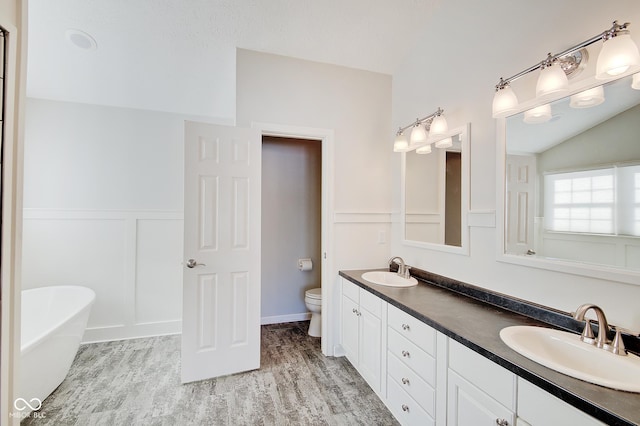 bathroom featuring hardwood / wood-style floors, vanity, vaulted ceiling, a washtub, and toilet