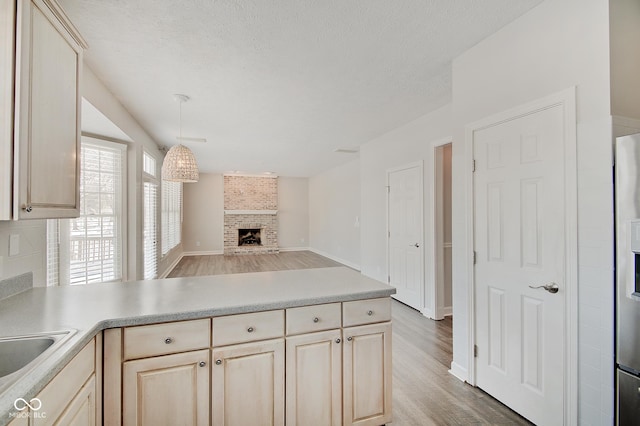 kitchen featuring light brown cabinetry, a textured ceiling, pendant lighting, hardwood / wood-style flooring, and a fireplace