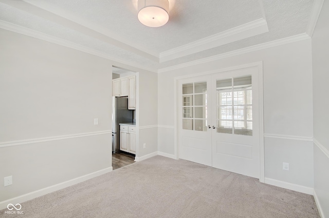 carpeted empty room with french doors, a textured ceiling, a tray ceiling, and ornamental molding