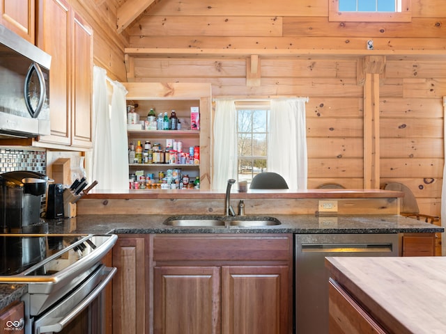 kitchen with appliances with stainless steel finishes, sink, dark stone countertops, and wood walls