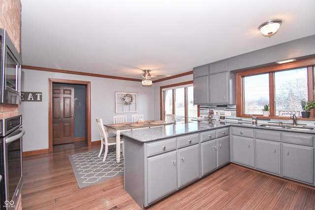 kitchen with gray cabinetry, sink, stainless steel appliances, kitchen peninsula, and hardwood / wood-style floors