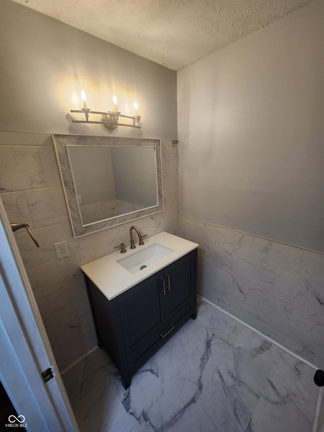 bathroom featuring vanity, a textured ceiling, and tile walls