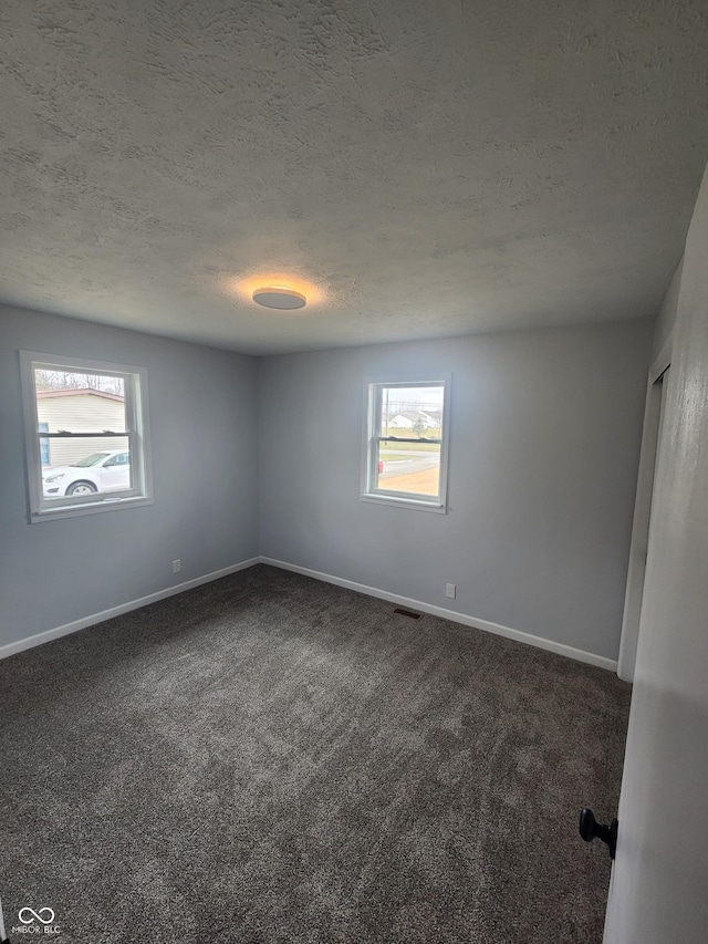 spare room featuring a wealth of natural light, a textured ceiling, and dark colored carpet