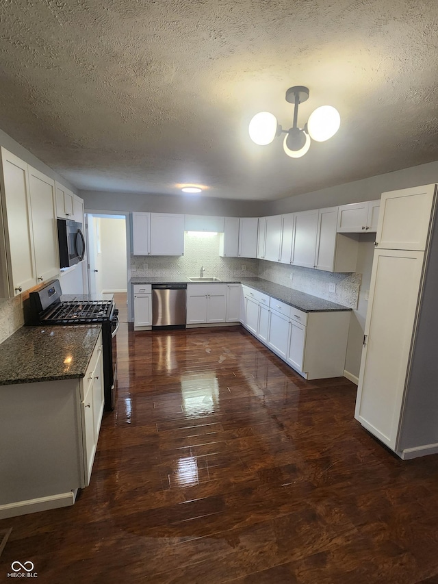 kitchen with white cabinets, stainless steel appliances, and dark stone counters