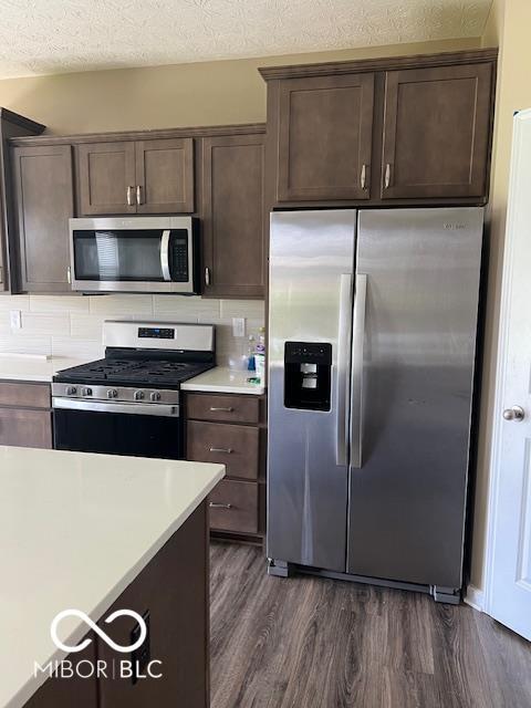 kitchen with dark hardwood / wood-style floors, a textured ceiling, tasteful backsplash, dark brown cabinetry, and stainless steel appliances