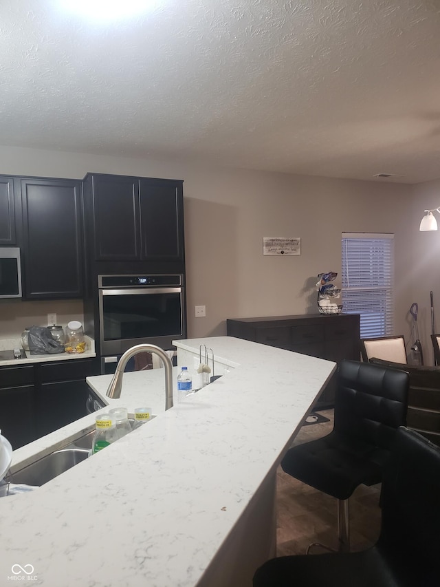 kitchen with stainless steel appliances, a textured ceiling, a breakfast bar, and sink