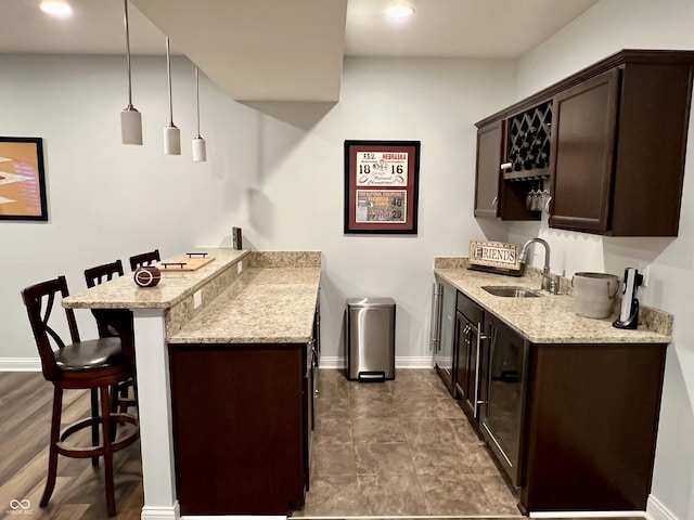 bar with dark brown cabinetry, light stone counters, sink, and decorative light fixtures