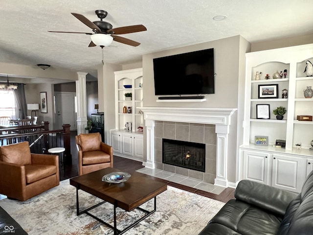 living room with a tiled fireplace, ceiling fan, light hardwood / wood-style flooring, and a textured ceiling