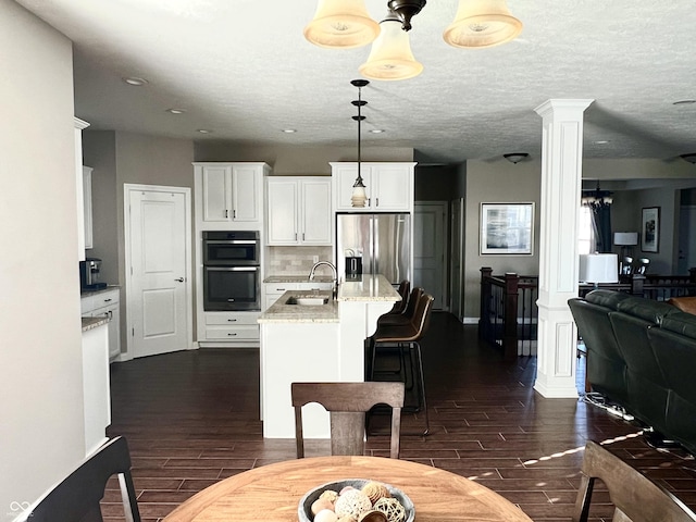 kitchen with appliances with stainless steel finishes, light stone counters, sink, white cabinets, and hanging light fixtures