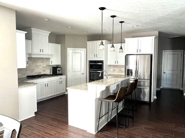 kitchen featuring white cabinets, hanging light fixtures, an island with sink, and stainless steel appliances