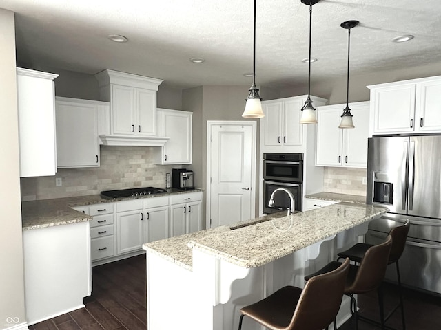 kitchen featuring a kitchen island with sink, white cabinetry, pendant lighting, and stainless steel appliances