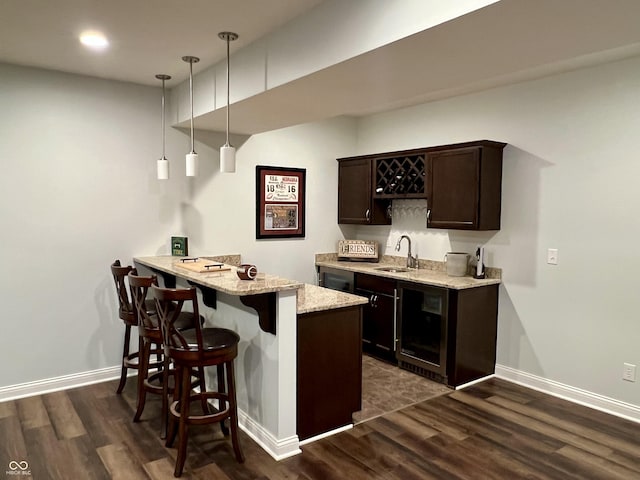 bar featuring sink, dark brown cabinetry, hanging light fixtures, and dark wood-type flooring