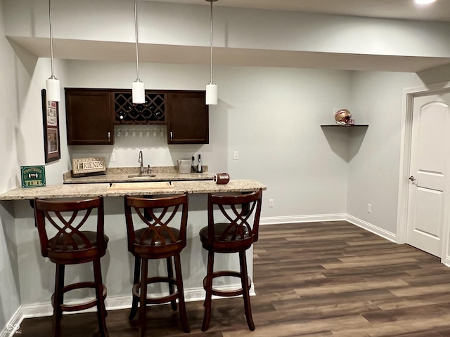 kitchen with light stone countertops, dark hardwood / wood-style flooring, dark brown cabinetry, hanging light fixtures, and a breakfast bar area