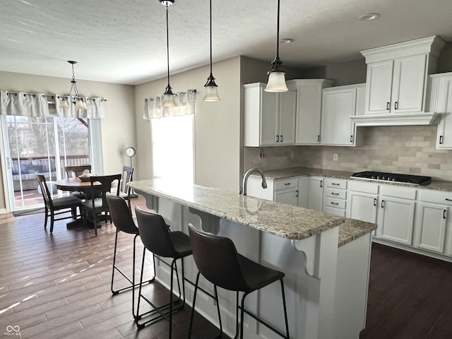 kitchen featuring gas cooktop, decorative backsplash, decorative light fixtures, white cabinetry, and a breakfast bar area