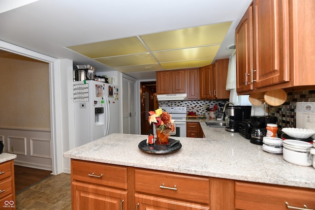 kitchen featuring backsplash, light stone counters, sink, and white appliances