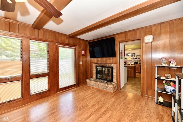 living room featuring ceiling fan, beamed ceiling, wooden walls, a fireplace, and light wood-type flooring