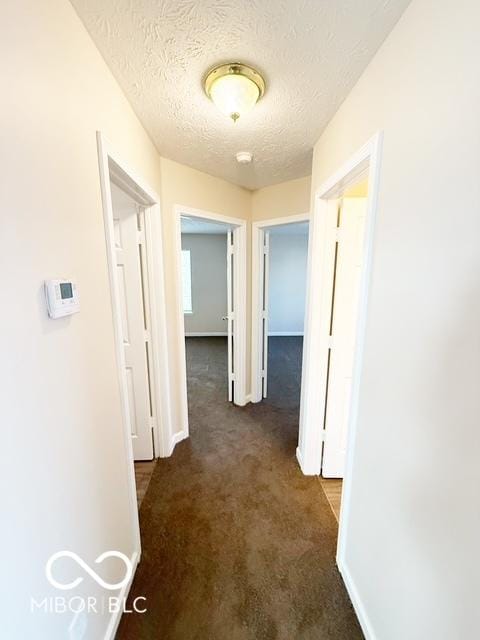 corridor featuring a textured ceiling and dark carpet