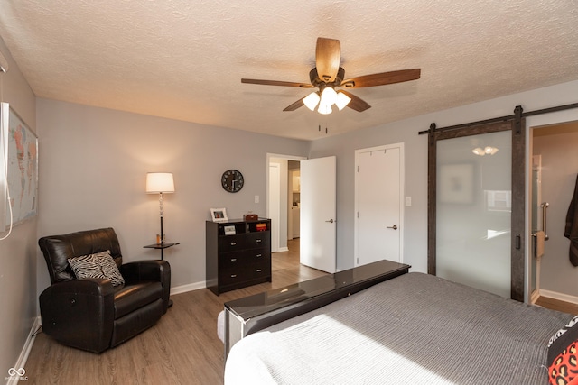 bedroom featuring hardwood / wood-style flooring, ceiling fan, a barn door, and a textured ceiling