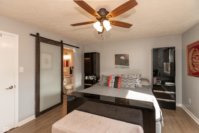 bedroom featuring hardwood / wood-style floors, a barn door, ensuite bathroom, and ceiling fan