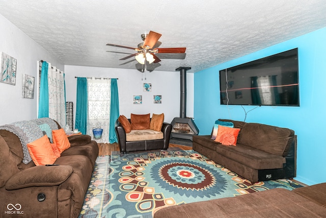 living room with hardwood / wood-style flooring, ceiling fan, a wood stove, and a textured ceiling