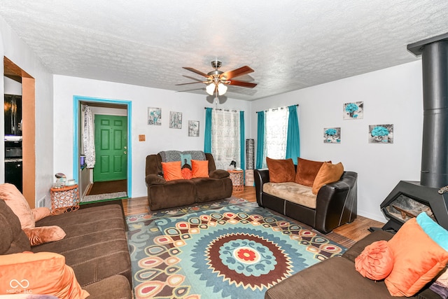 living room featuring a wood stove, ceiling fan, hardwood / wood-style floors, and a textured ceiling