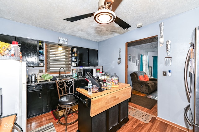 kitchen featuring ceiling fan, sink, stainless steel fridge, a textured ceiling, and hardwood / wood-style flooring