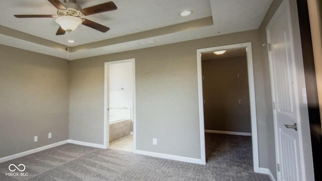 unfurnished bedroom with carpet, a walk in closet, a tray ceiling, ceiling fan, and a closet