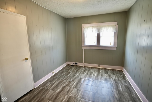 spare room with dark hardwood / wood-style flooring, wooden walls, and a textured ceiling