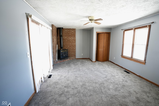 unfurnished living room featuring carpet, a textured ceiling, ceiling fan, and a wood stove