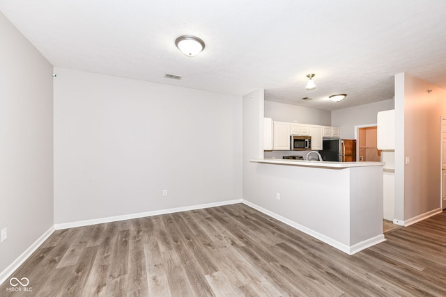 kitchen with white cabinetry, kitchen peninsula, stainless steel appliances, and light hardwood / wood-style flooring